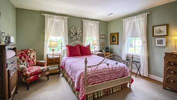 A bedroom with a four-poster bed, a floral armchair, a dresser, and a nightstand with a lamp.
