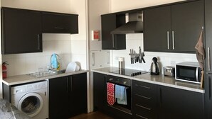 A modern kitchen with black cabinets, a washing machine, a microwave, and a kettle. - Moray Hastings (Hastings)
