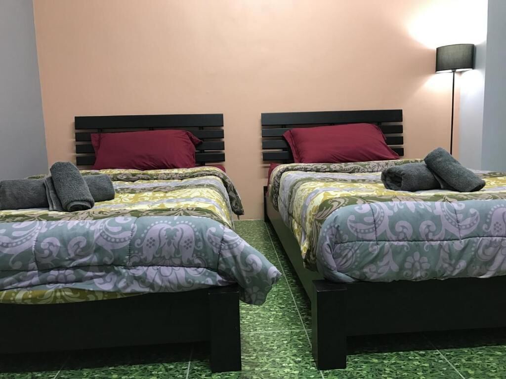 Two twin beds with patterned bedding, a dark headboard, and a green tiled floor.
