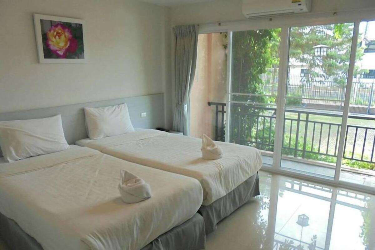 A hotel room with two beds, a large window with a view of greenery, and an air conditioning unit on the wall.