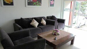 A living room with a sofa and armchairs, a coffee table with a floral arrangement, and framed floral artwork on the wall. - Rose Villa Resort (Pak Chong)