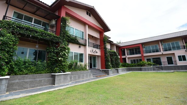 A multi-story hotel with a red and beige facade, a balcony on the second floor, and a well-maintained lawn in front. - Rose Villa Resort (Pak Chong)