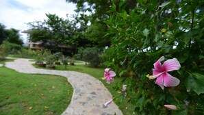 A stone pathway leading through a garden with lush greenery and pink flowers. - Rose Villa Resort (Pak Chong)