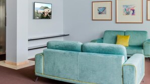 Ein smaragdgrünes Sofa mit gelben Kissen, einem aufgehängten Bilderrahmen und einem eingebauten Regal.
