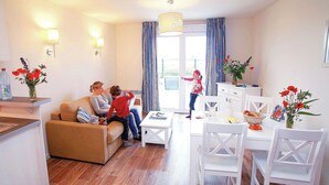 Ein Wohnzimmer mit einer Couch, einem Esstisch mit Stühlen, einer Küchenzeile und einem Fenster mit Vorhängen.