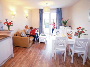 Ein Wohnzimmer mit einer Couch, einem Esstisch mit Stühlen, einer Küchenzeile und einem Fenster mit Vorhängen.