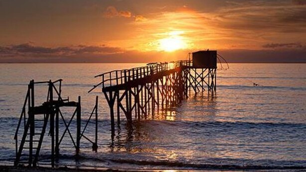Eine Pier, die sich in ruhiges Wasser bei Sonnenuntergang erstreckt.