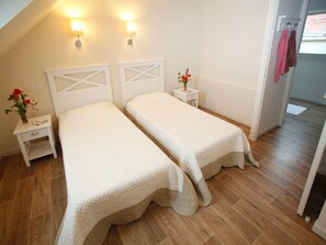 Ein Zimmer mit zwei Betten, einem Nachttisch mit Blumenvase und einer Wandlampe.