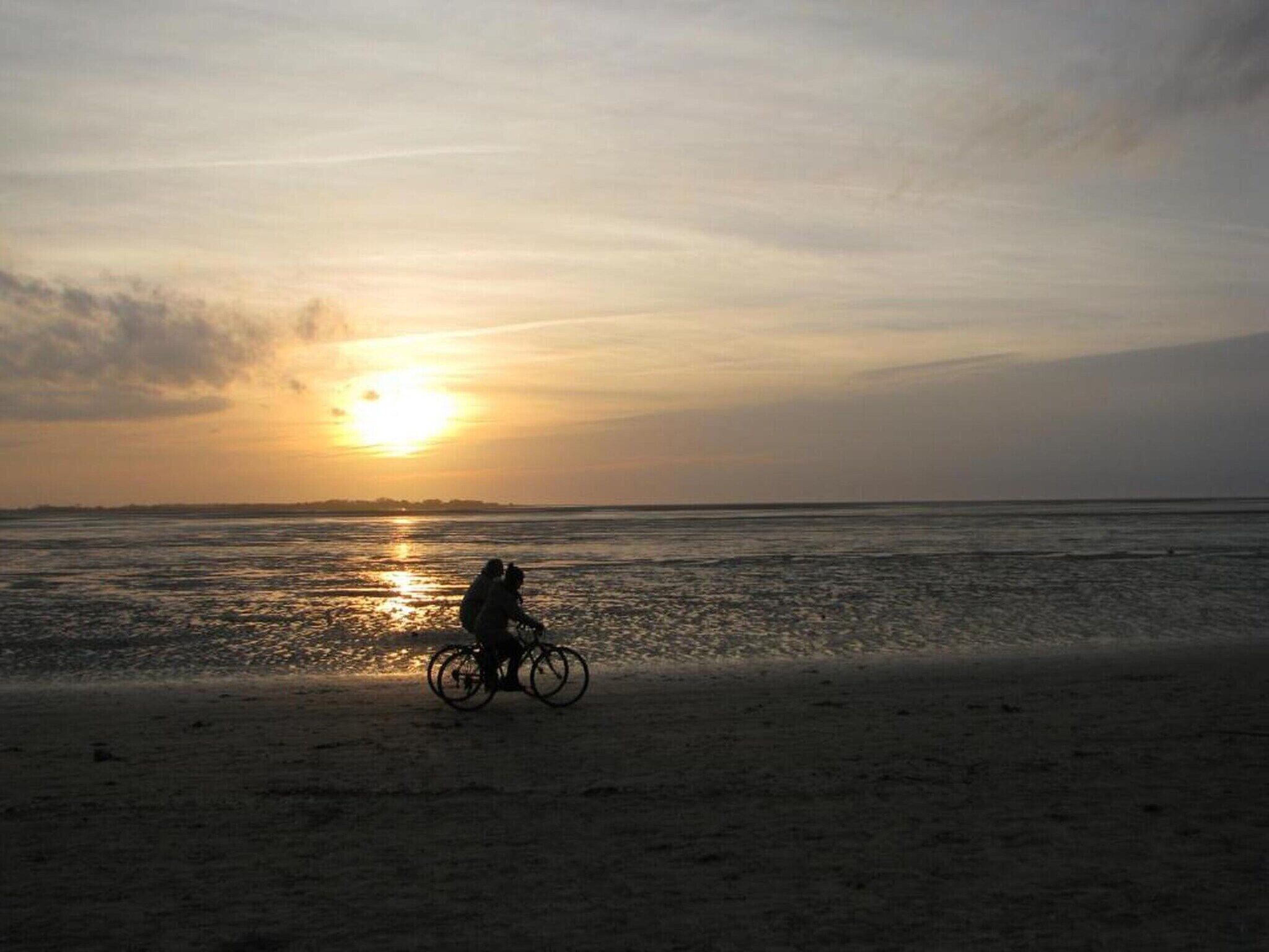 Escena de playa con una persona montando bicicleta cerca del agua durante el atardecer.