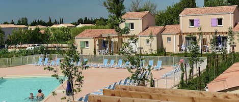 Un resort con piscina, tumbonas y villas con tejados rojos.