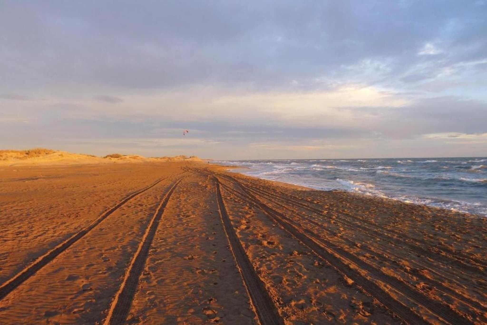 Una playa con un sendero arenoso que lleva al agua, bajo un cielo nublado.