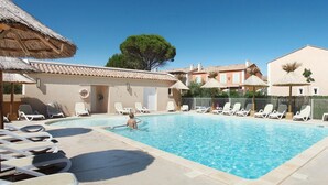 Una piscina con sillas de descanso y una estructura de techo de paja.