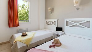 Una habitación con dos camas, una ventana con cortinas, un ordenador portátil sobre una mesita y una lámpara fijada a la pared.