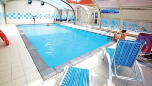 An indoor swimming pool with clear water, surrounded by lounge chairs and a covered area with a checkered wall. - Relaxing Coastal Apt for 8 (le Crotoy)