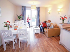 Ein modernes Wohnzimmer mit Sofa, Esstisch und Stühlen. Es gibt eine Küchenzeile mit Arbeitsplatte und einem Fenster.