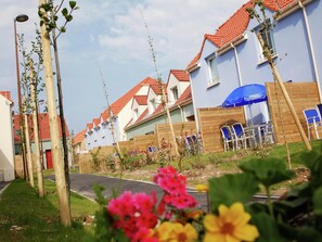 A row of residential buildings with red-tiled roofs, wooden fences, and a blue umbrella.