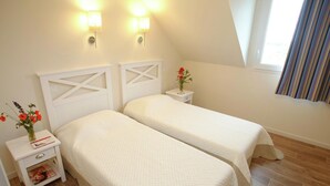 A bedroom with two beds, a nightstand with a lamp, and a window with curtains. - Relaxing Coastal Apt for 8 (le Crotoy)