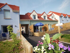 A row of villas with red-tiled roofs, a covered entrance, and a sign indicating availability.