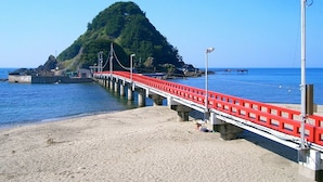 A beach with a red and white pier extending into the water, a sandy shore, and a green hill in the background.