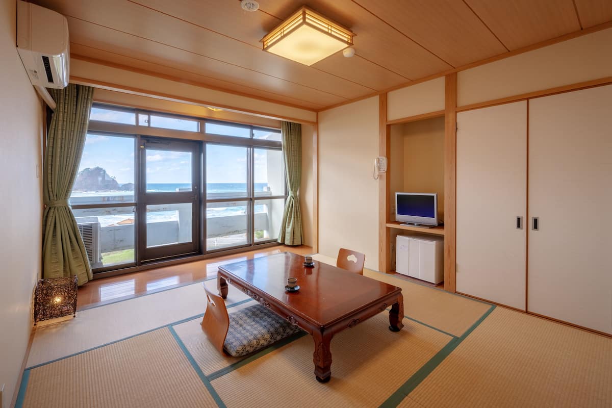 Een traditionele Japanse kamer met tatami vloerbedekking, een houten tafel, een televisie en uitzicht op de zee.