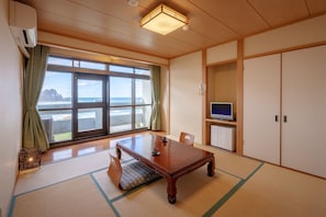 A traditional Japanese room with tatami flooring, a wooden table, a television, and a view of the sea. - Hotel Sunresort Shonai (Tsuruoka)