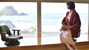 A person sitting by a window with a view of the sea and buildings.