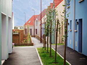A narrow residential street with houses on both sides, a grassy median, and a clear sky.