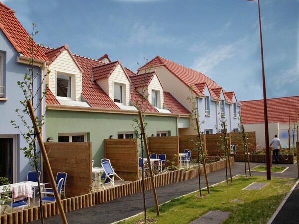 A row of modern houses with red-tiled roofs, wooden fences, and outdoor seating areas.