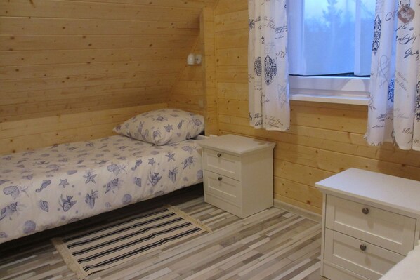 Una habitación pequeña y acogedora con detalles de madera, una cama individual con colcha estampada, una mesita de noche y una ventana con cortinas.