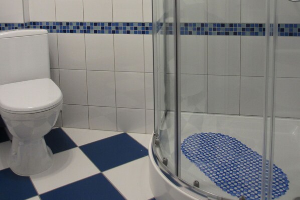 Un baño con inodoro blanco, cabina de ducha de vidrio y suelo a cuadros.