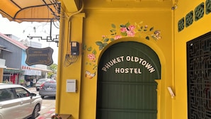 Entrada de un hostal con un cartel que dice "Phuket Oldtown Hostel" y una puerta verde.
