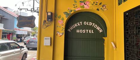 A hostel entrance with a sign reading "Phuket Oldtown Hostel" and a green door.