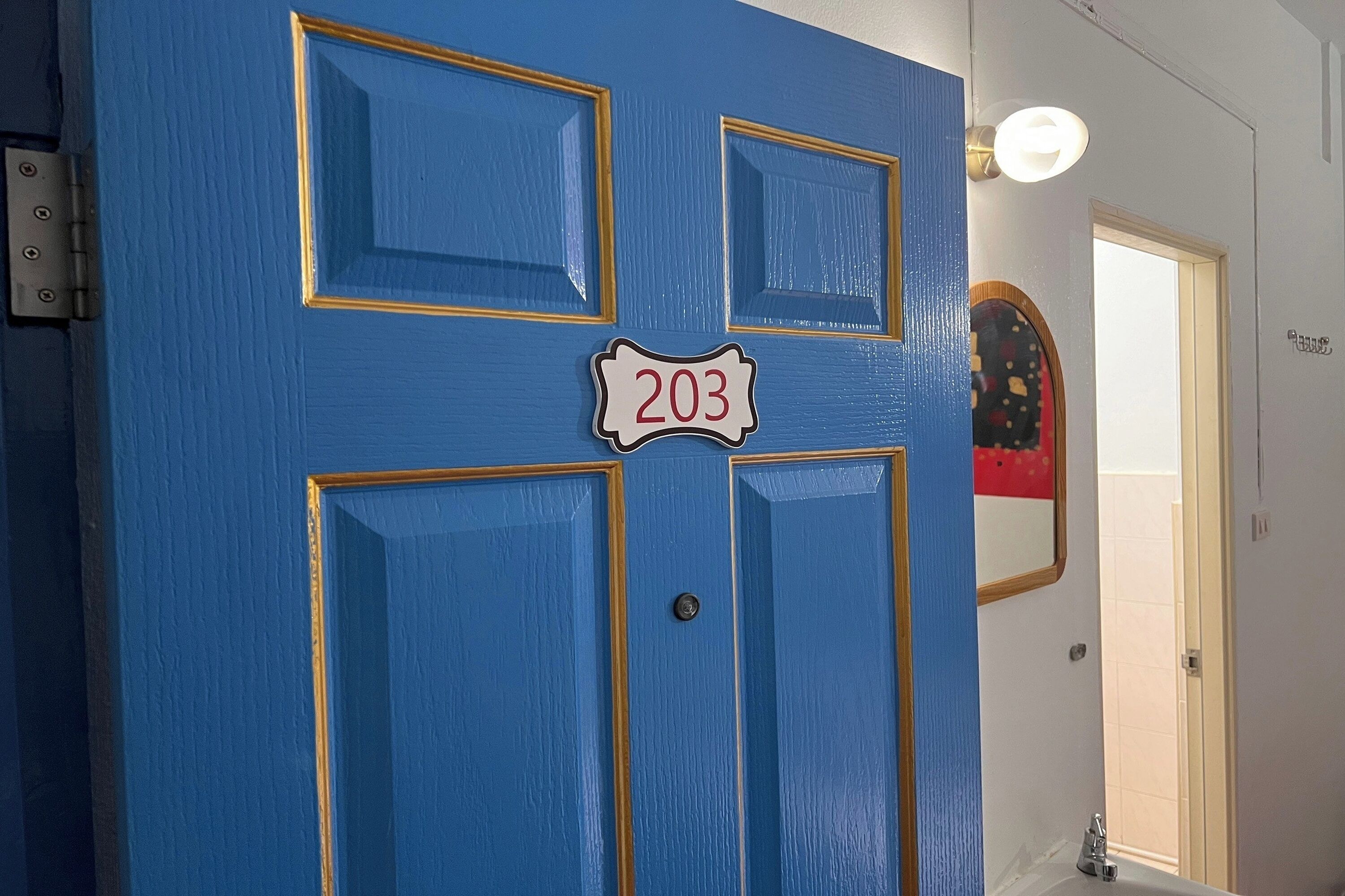 A blue door with the number 203, a light fixture, and a small mirror on the wall.