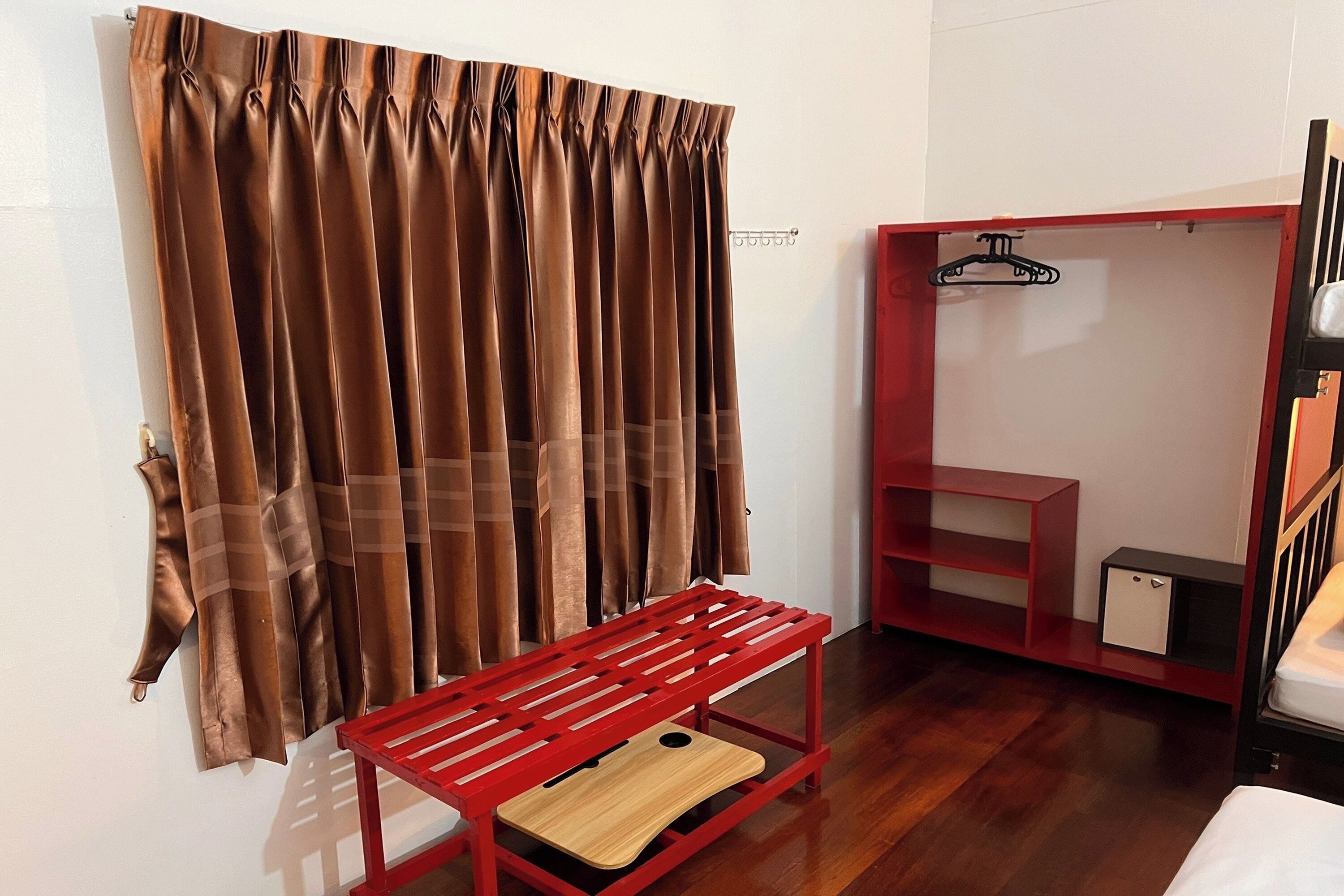 A room with a wooden bench, a red wardrobe, and a hanging coat rack.