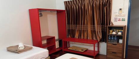 A hotel room with two beds, a red wardrobe, a wooden shelf with toiletries, and a curtain.