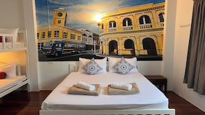 Habitación de hotel con cama, dos almohadas, mesita de noche y un mural en la pared con la imagen de un edificio.