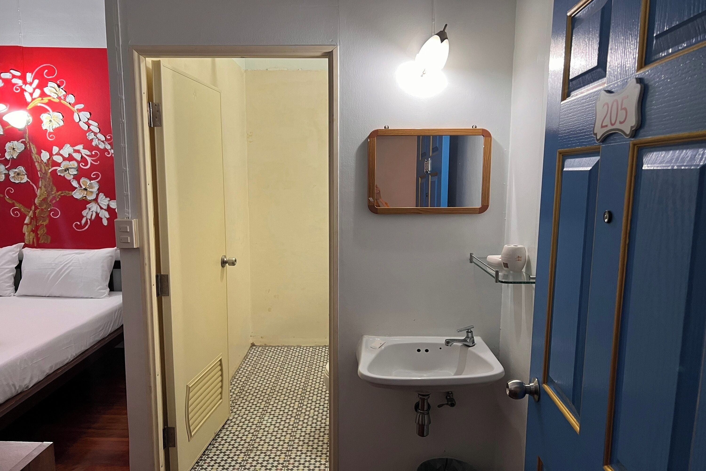A hotel room with a bed, a bathroom with a sink and mirror, and a door with the number 205.