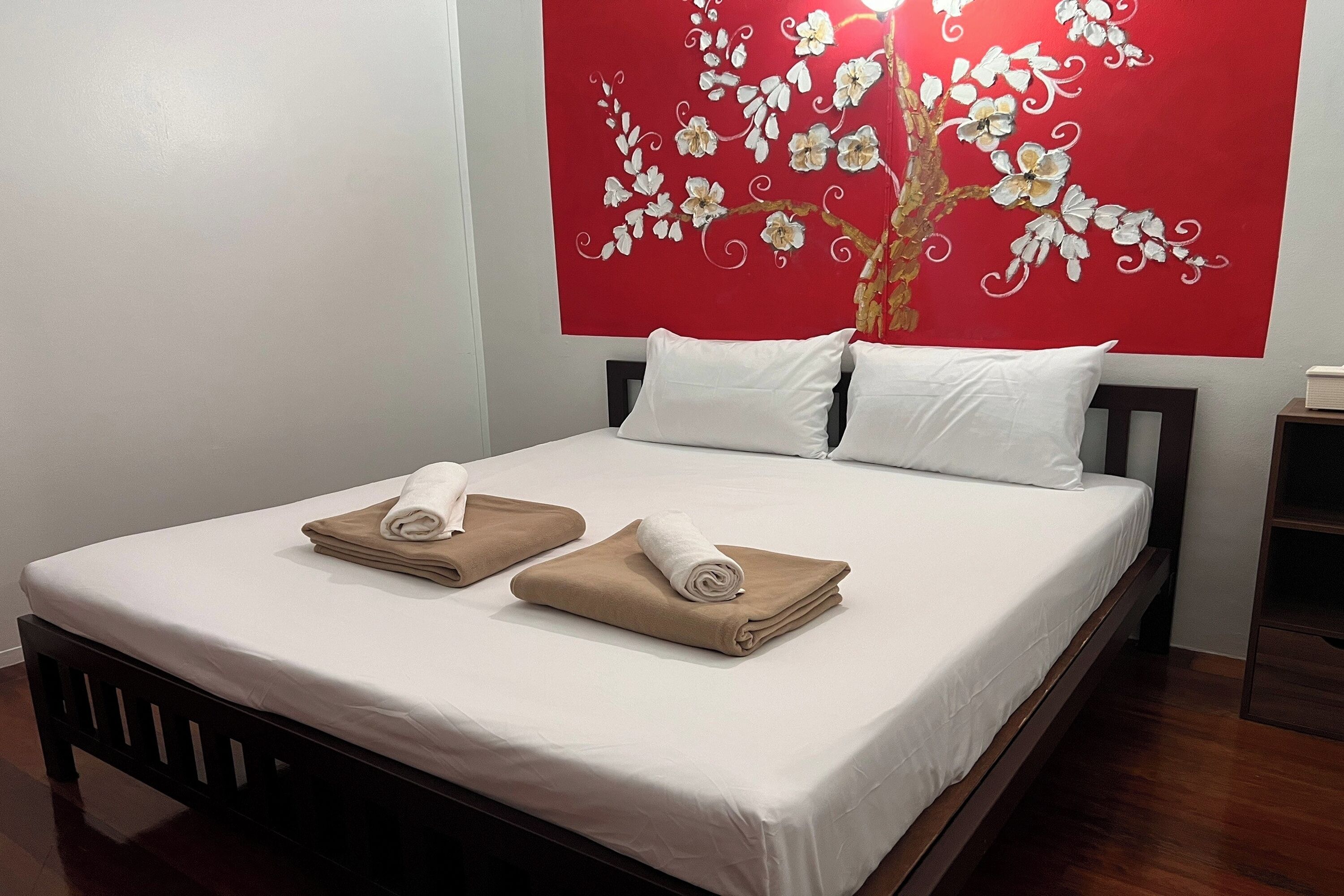 Een netjes opgemaakt bed met witte en beige handdoeken, een bloemenkunstwerk in rood en een houten hoofdbord.