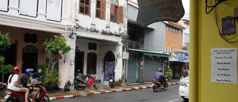 Vista de la calle con un letrero del Phuket Old Town Hostel, que indica los tipos de habitaciones y la información de contacto.