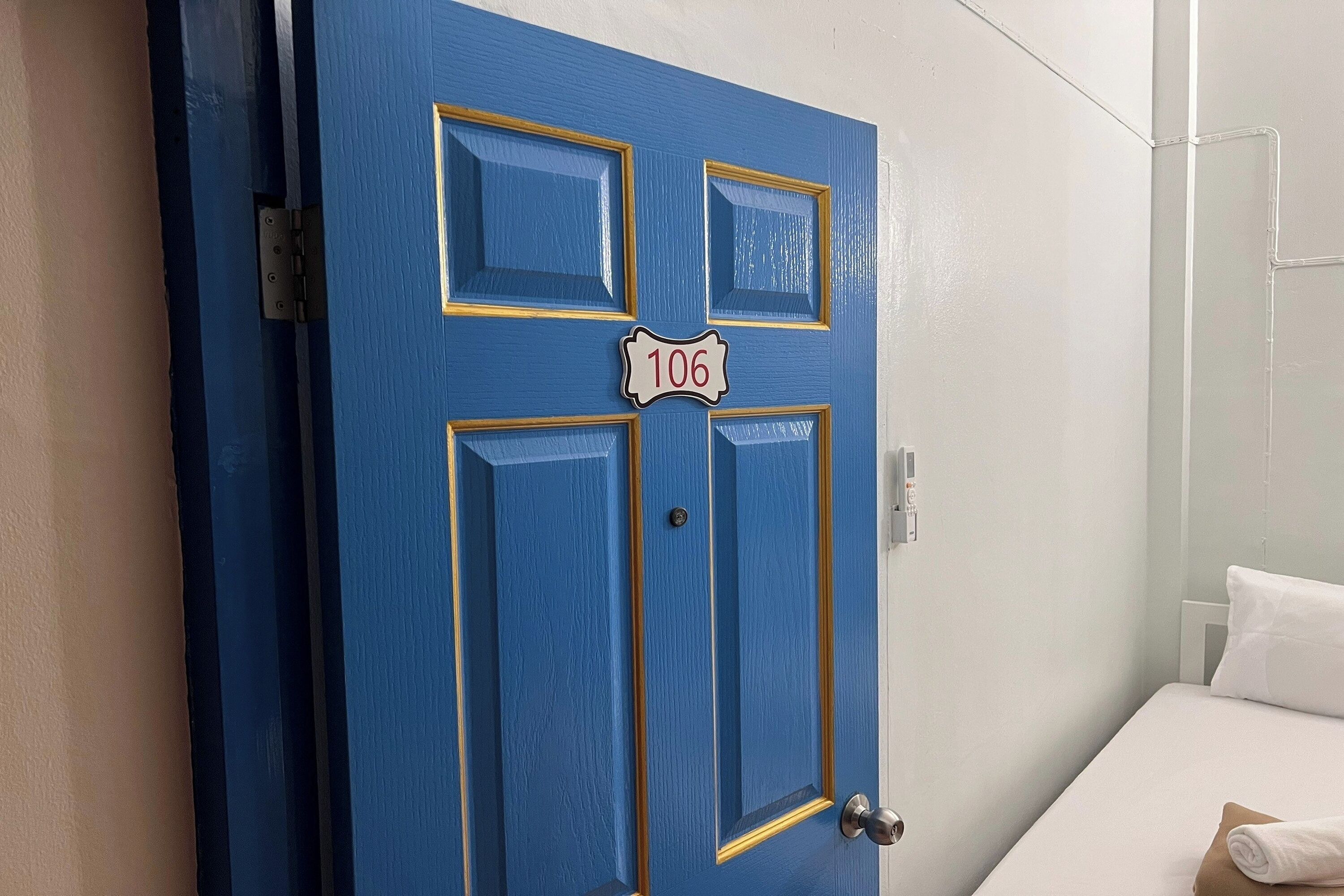 A blue door with the number 106, a white wall, and a bed with a white pillow.