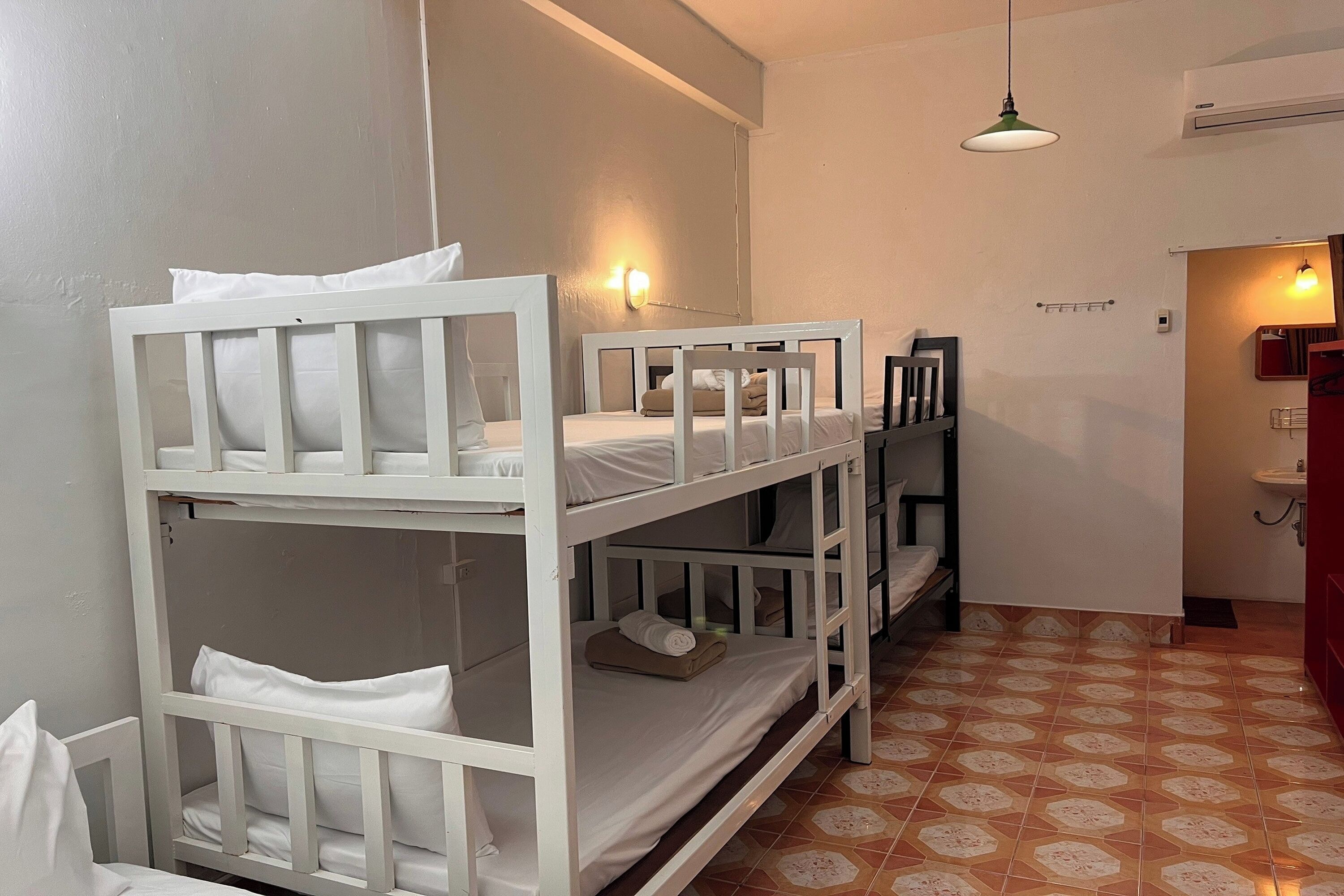 A room with bunk beds, a hanging light, a tiled floor, and a small bathroom area.