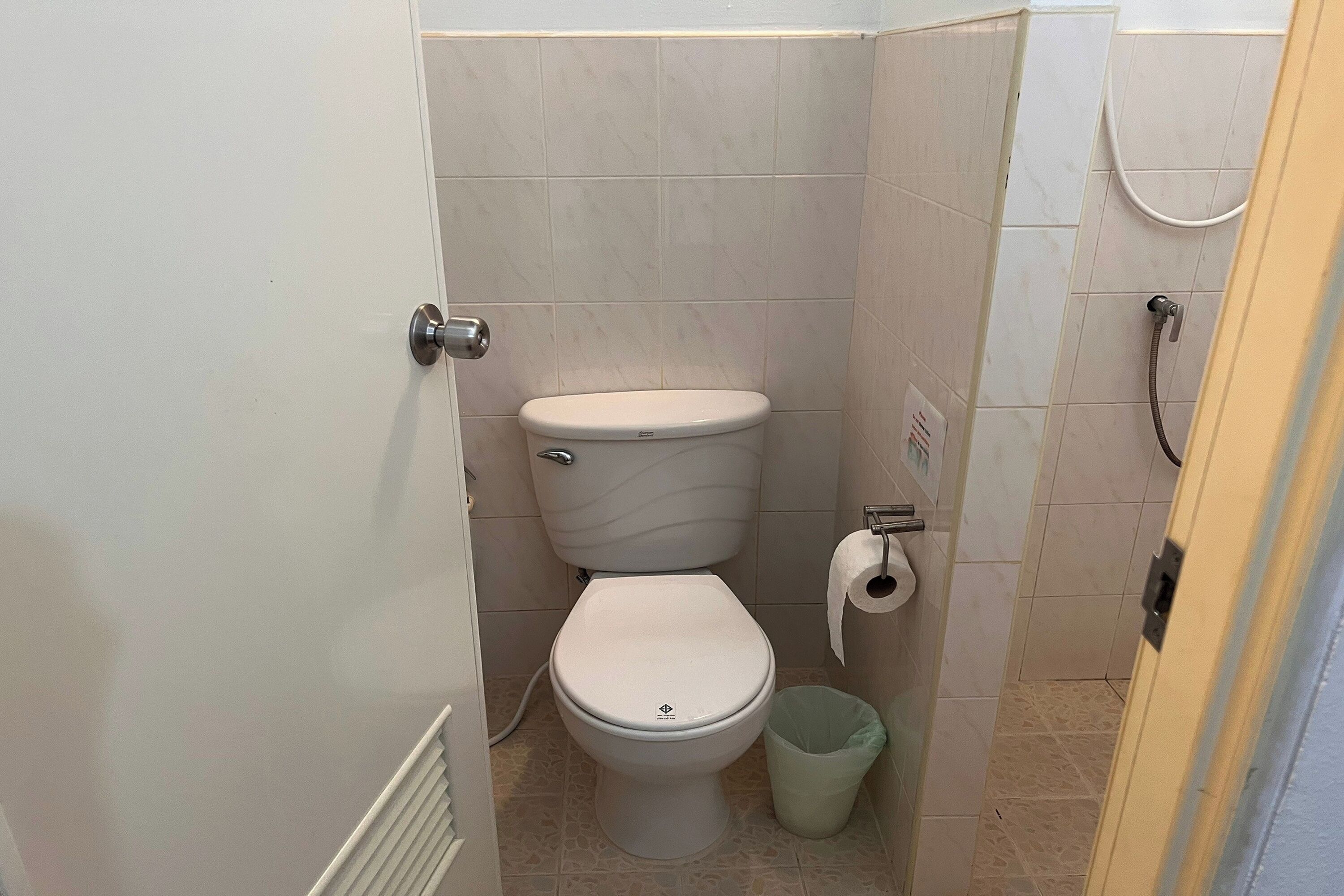 A small, compact bathroom with a toilet, a trash bin, and a shower area.