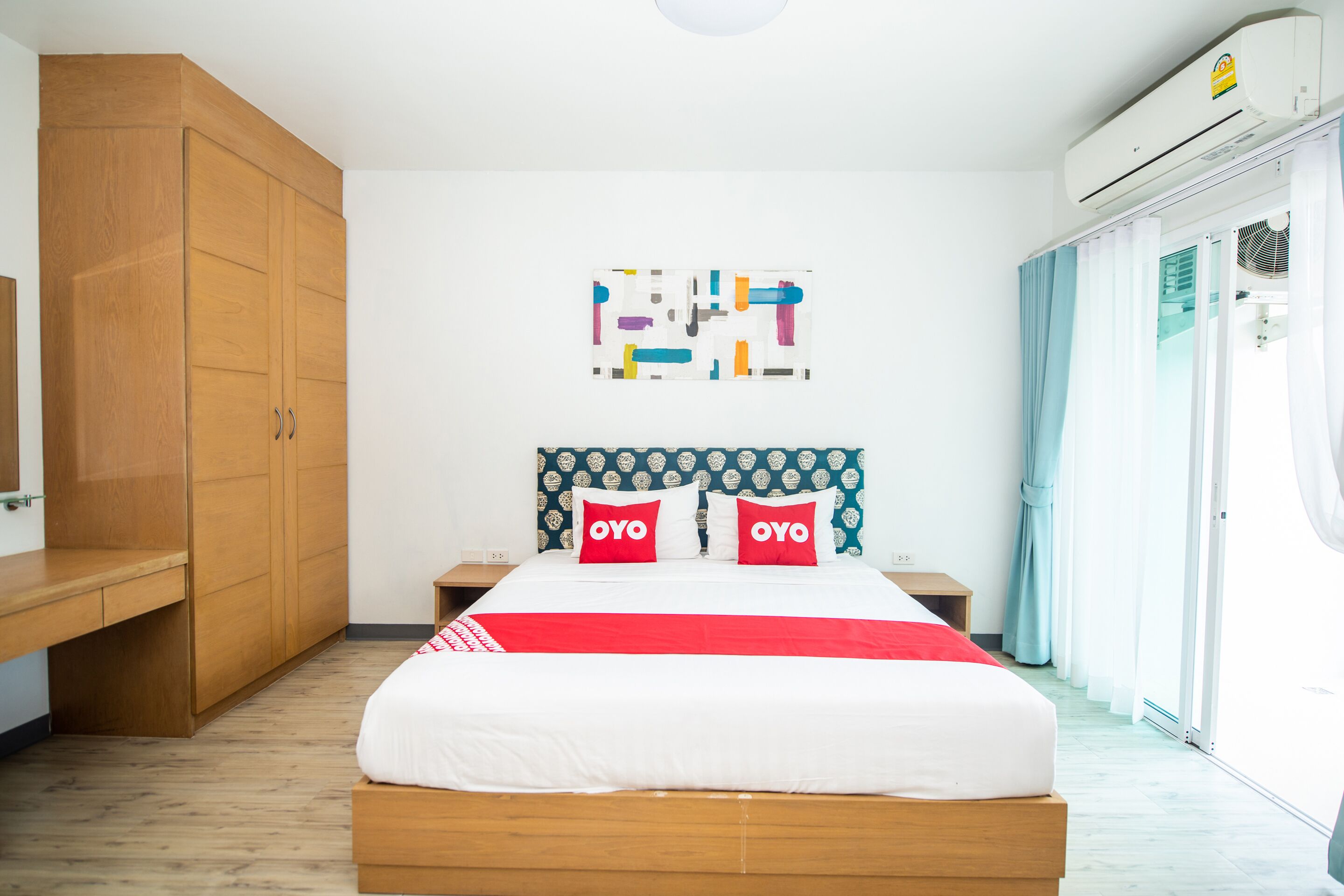 A hotel room with a wooden bed, a large wardrobe, a wall art piece, and a sliding glass door to the outside.