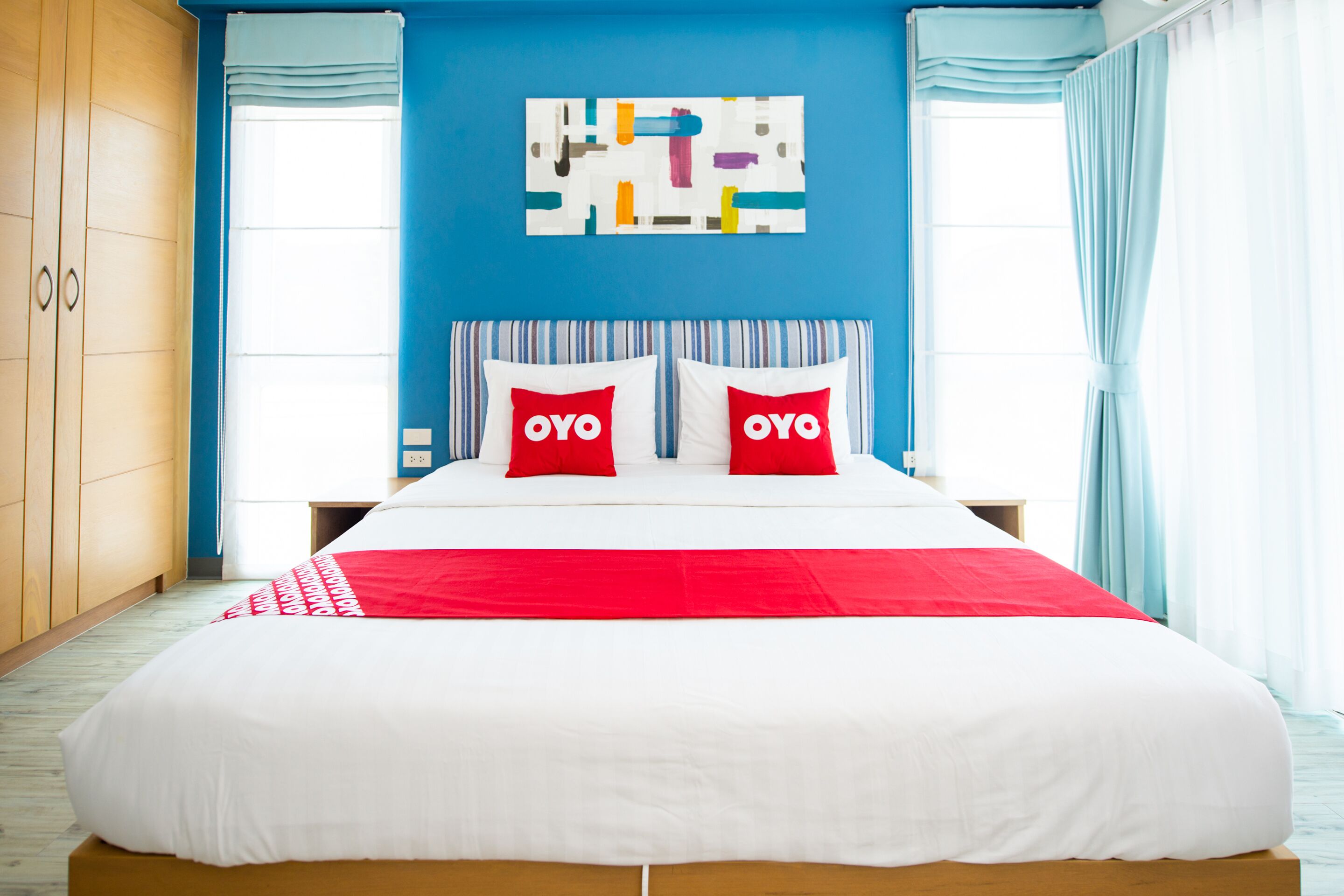 Un dormitorio con una cama grande, una pared de acento azul y una obra de arte abstracto sobre la cama.