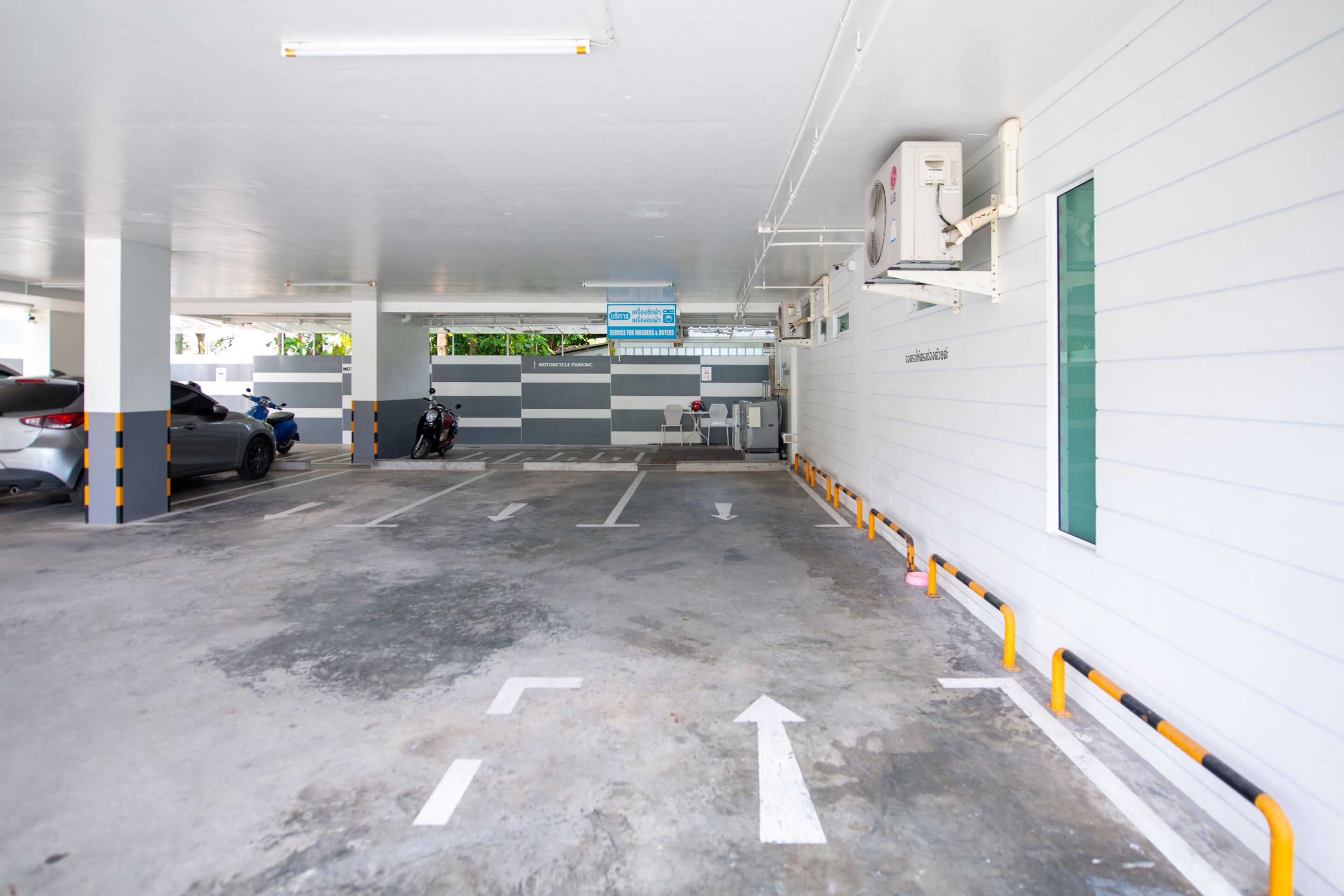 Un estacionamiento con flechas direccionales en el suelo, un letrero azul y una motocicleta estacionada cerca de la entrada.