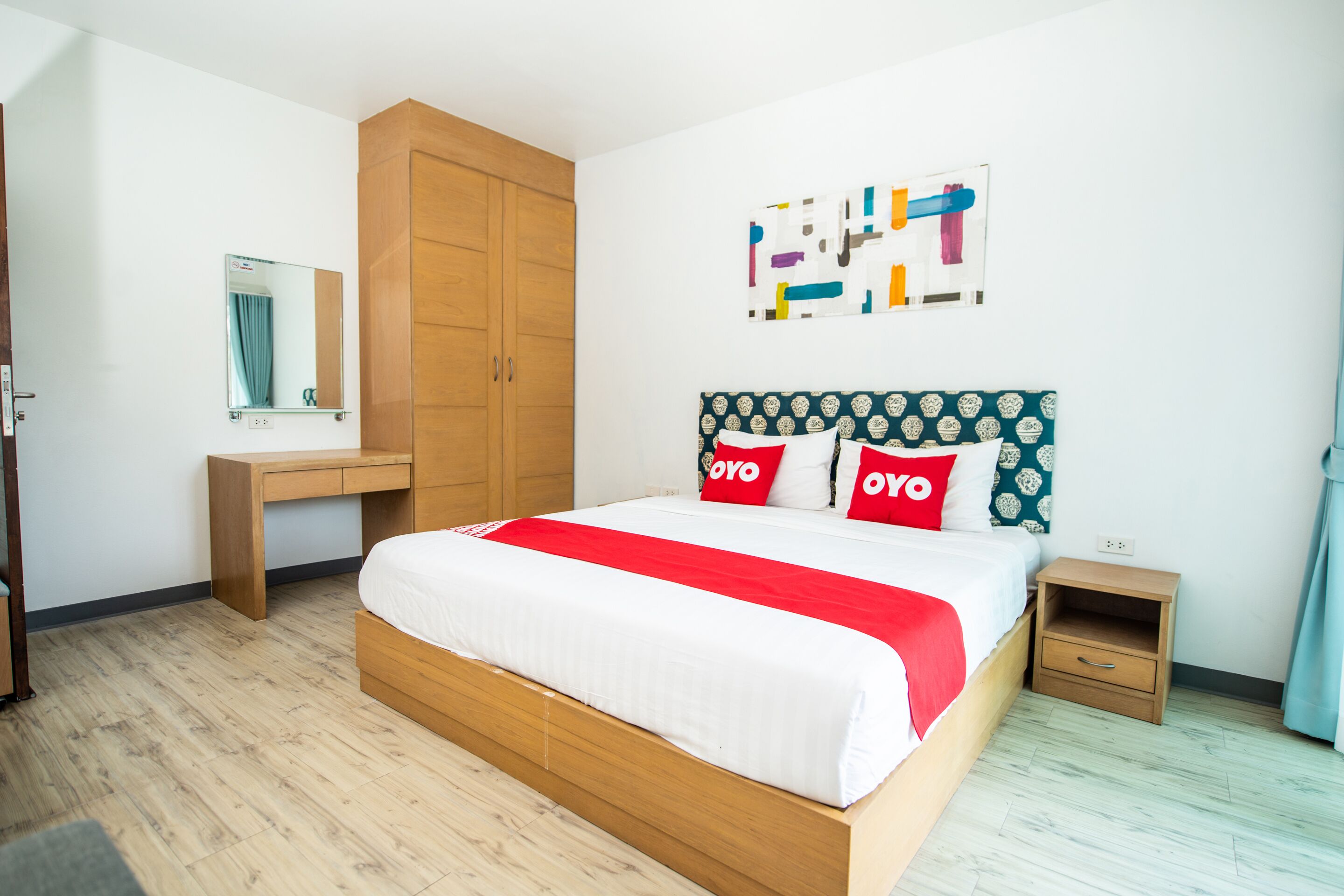 A bedroom with a wooden bed, a desk, a wardrobe, and a wall-mounted mirror.