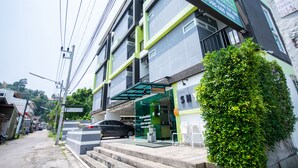 Un edificio de varios pisos con fachada verde y blanca, una escalera visible que lleva a la entrada y un coche estacionado al frente.