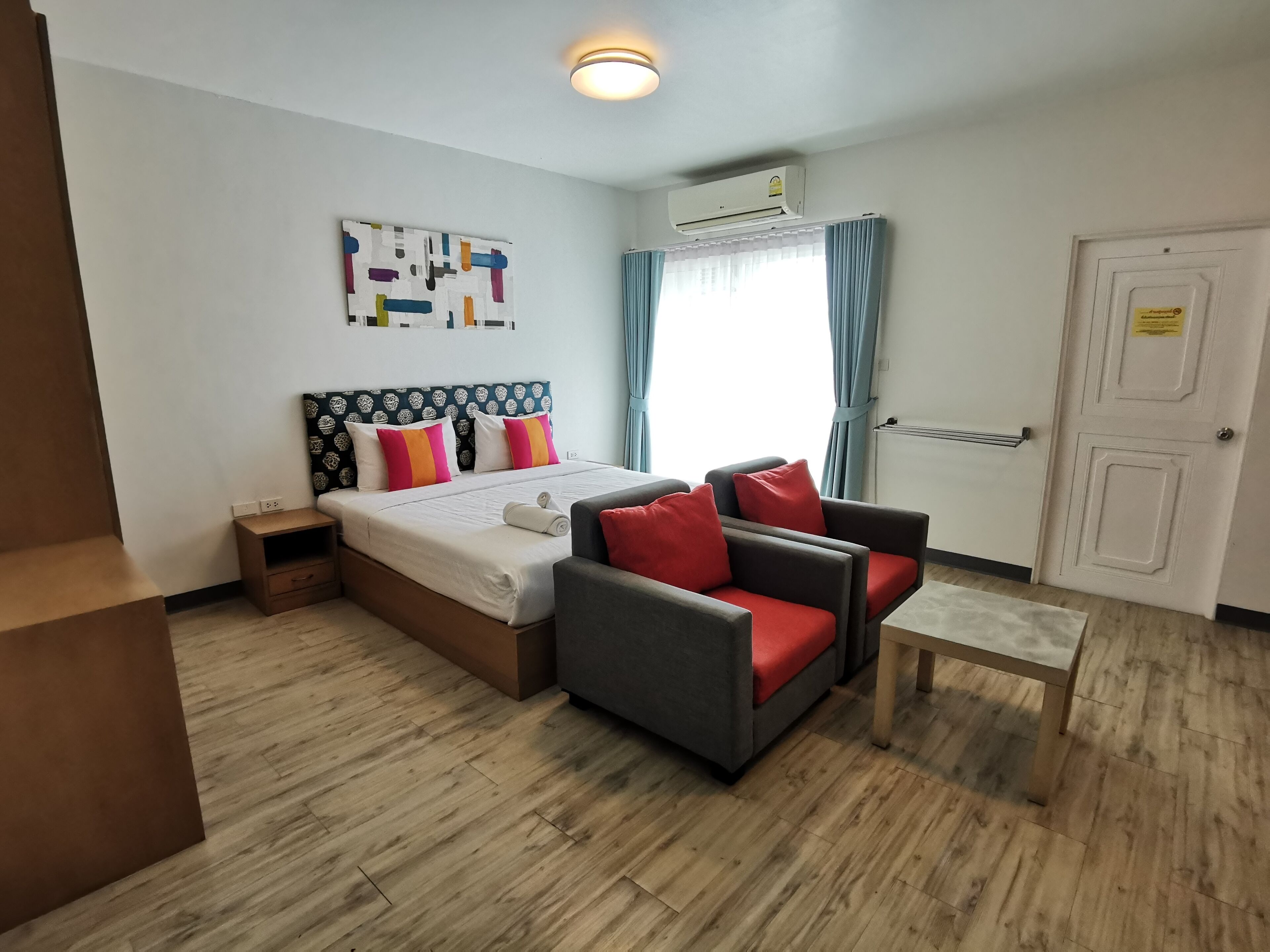 A hotel room with a bed, a sofa, a small table, and a wall-mounted air conditioner.