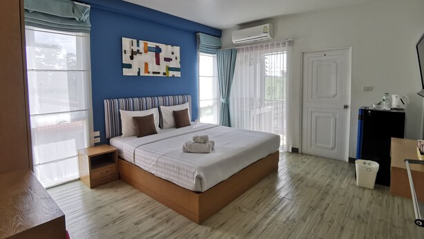 Un dormitorio con cama, ventana con cortinas, puerta, equipo de aire acondicionado y una mesita con hervidor.