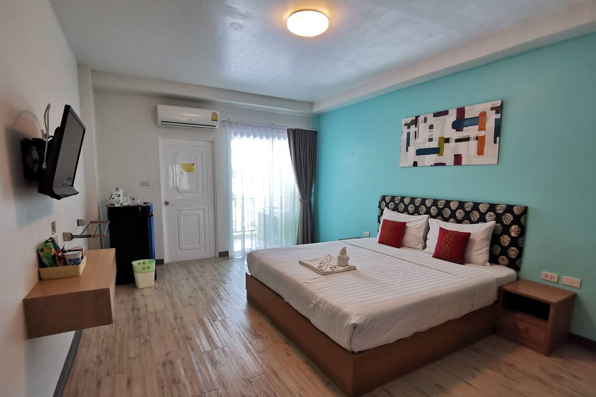 Habitación de hotel con una cama grande, un televisor montado en la pared, un escritorio con una computadora y una ventana con cortinas.
